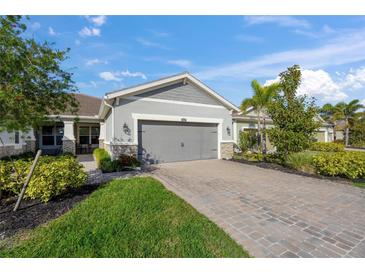 Single-story home with gray garage door and paver driveway; landscaping includes lush green grass and bushes at 8669 Rain Song Rd, Sarasota, FL 34238