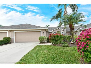 Tan house with two-car garage, lush landscaping, and palm trees at 5150 Mahogany Run Ave, Sarasota, FL 34241