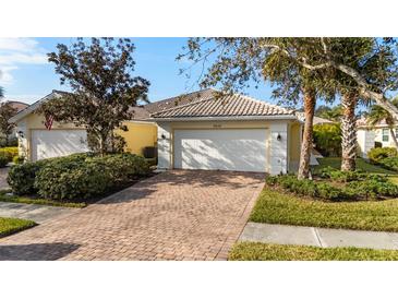 Charming home featuring a white garage door, tile roof, brick driveway, and beautifully manicured landscaping at 8849 Etera Dr, Sarasota, FL 34238