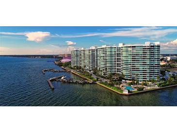 Beautiful aerial view of white condo buildings with docks, palm trees and a pool, against a blue water backdrop at 888 Blvd Of The Arts # 1608, Sarasota, FL 34236