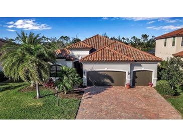 Beautiful home featuring a two-car garage, barrel tile roof and a brick paved drive framed by lush landscaping at 13303 Swiftwater Way, Lakewood Ranch, FL 34211