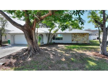 Charming home featuring an attractive stone accent wall, a well-manicured lawn, and mature shade trees at 22151 Lancaster Ave, Port Charlotte, FL 33952