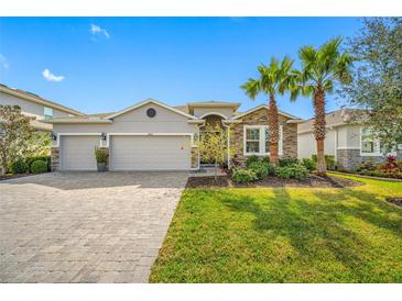 Charming single-story home featuring stone accents, three-car garage, lush lawn, and beautiful palm trees at 5821 Hevena Ct, Palmetto, FL 34221