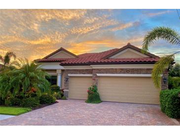 Charming home featuring a red tile roof, stone accents, lush landscaping, and a paver driveway, all under a vibrant sunset sky at 20909 Loggia Ct, Venice, FL 34293