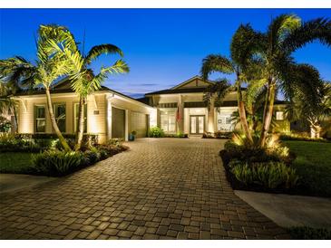 Beautiful home exterior with a brick driveway, lush landscaping, and warm lighting at twilight at 8271 Redonda Loop, Lakewood Ranch, FL 34202