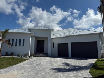 An elegant front exterior with a paved driveway, metal roof, black front doors and a three-car garage at 1426 Mineo Dr, Punta Gorda, FL 33950