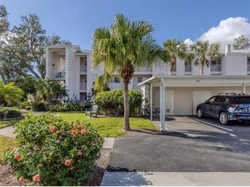 Inviting condo exterior with carport, lush landscaping, and a neatly maintained lawn under a sunny, clear sky at 437 Cerromar Ln # 312, Venice, FL 34293