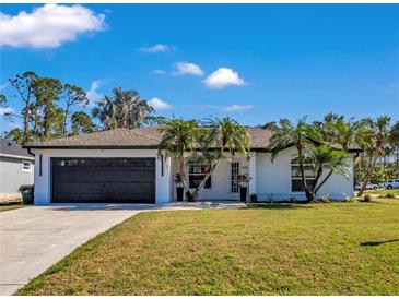 White house with black garage door, palm trees, and a well-manicured lawn at 2418 Frantz St, North Port, FL 34286