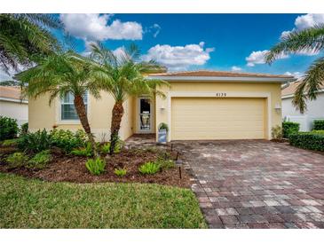Bright yellow house with palm trees, brick driveway and well-manicured landscaping at 6139 Grand Cypress Blvd, North Port, FL 34287