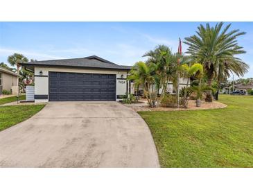 Beautiful home with a landscaped lawn, palm trees, and a dark-colored garage door at 7424 S Moss Rose, Punta Gorda, FL 33955