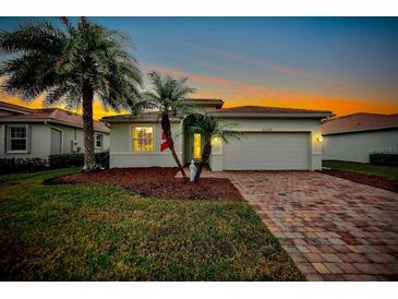 Charming one-story home with a brick driveway and palm trees during sunset at 6049 Grand Cypress Blvd, North Port, FL 34287