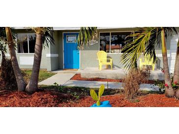 Charming house with a blue door and yellow chairs on the porch, surrounded by tropical landscaping at 18086 Clanton Ave, Port Charlotte, FL 33948