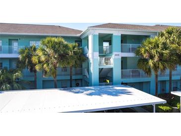 Building exterior, featuring light teal paint, palm trees, and covered parking at 19375 Water Oak Dr # 203, Port Charlotte, FL 33948