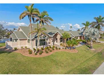 Stunning exterior view of a single-story home with lush landscaping and mature palm trees against a blue sky at 1701 Casey Key Dr, Punta Gorda, FL 33950
