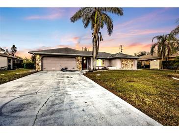 Single-story home with concrete driveway, two car garage, stone accents, and mature landscaping at 26166 Paysandu Dr, Punta Gorda, FL 33983