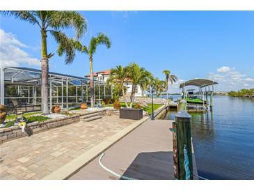 Waterfront home featuring a private dock, boat lift, and outdoor patio surrounded by lush landscaping and palm trees at 5196 Early Ter, Port Charlotte, FL 33981