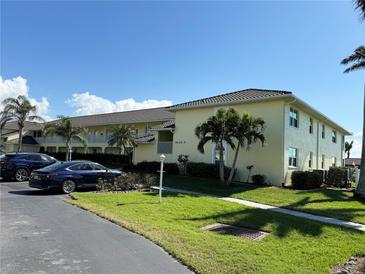 Well maintained yellow condo building with lush green lawn, palm trees, and parked vehicles at 4000 Bal Harbor Blvd # 527, Punta Gorda, FL 33950