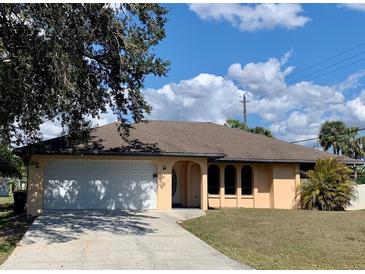 Charming home with a two-car garage, light yellow paint, an arched entryway, and a well-maintained lawn at 20408 Andover Ave, Port Charlotte, FL 33954