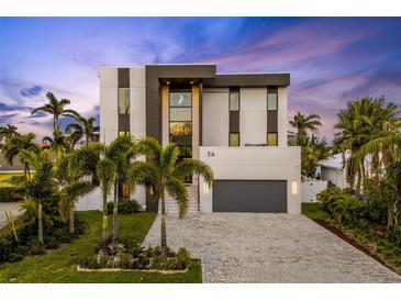 Striking modern home featuring a three-story facade, complemented by a gray driveway and lush tropical landscaping at 36 Dolphin Dr, Treasure Island, FL 33706
