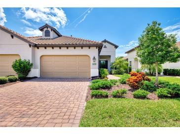 Charming home with a brick driveway, beige garage door, terra cotta roof, and lush landscaping at 26950 Pavin Dr, Englewood, FL 34223