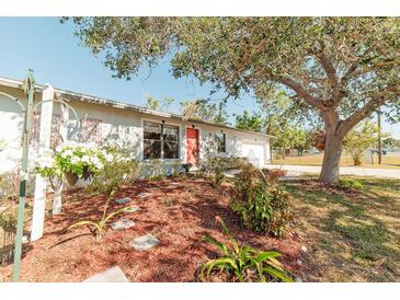 Charming house with a well-manicured lawn, mature tree, and inviting red door at 700 Coquina Ct, Nokomis, FL 34275