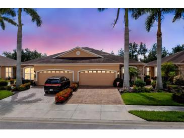 Tan house with three-car garage, landscaping, and palm trees at dusk at 4370 Turnberry Cir, North Port, FL 34288