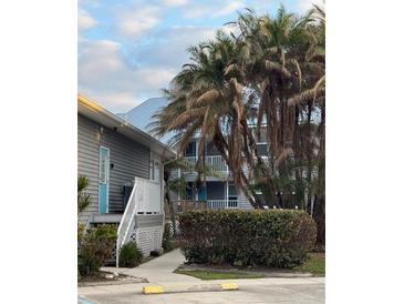 Gray building exterior with teal door, walkway, and lush landscaping, including palm trees at 4410 Warren Ave # 107, Port Charlotte, FL 33953