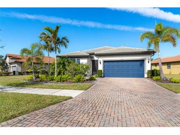 Single-story home with landscaped yard, paver driveway, and a blue garage door at 1506 Hyssop Loop, North Port, FL 34289