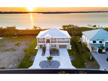 Stunning waterfront home featuring lush landscaping, a metal roof, and a grand staircase leading to the main entrance at 9861 Eagle Preserve Dr, Englewood, FL 34224