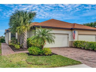 Well-maintained house with a two-car garage, lush landscaping, and a brick paved driveway at 9852 Haze Dr, Venice, FL 34292