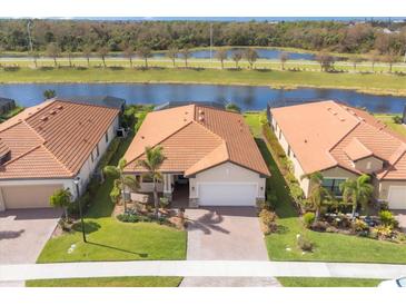 Three homes with terracotta roofs and landscaped yards, situated near a lake at 10133 Colubrina Dr, Venice, FL 34293