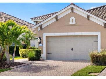 Tan house with two-car garage, landscaping, and brick driveway at 21621 Winter Park Ct, Venice, FL 34293