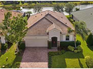 One-story home with tile roof, brick driveway, and landscaped lawn. Water view at 2049 Mesic Hammock Way, Venice, FL 34292