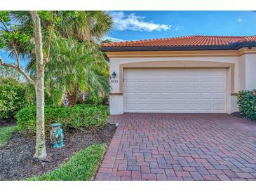 White garage door with red brick paver driveway and lush landscaping at 9855 Haze Dr, Venice, FL 34292