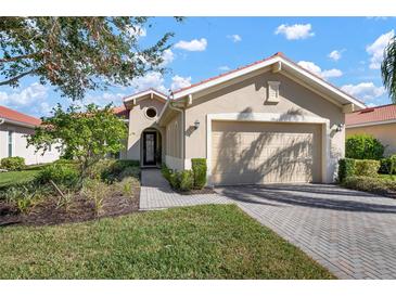 Tan single-story home with a two-car garage and landscaped lawn at 115 Avalini Way, North Venice, FL 34275