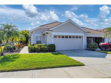 Tan house with two-car garage, lush landscaping, and a paved walkway at 1891 San Silvestro Dr, Venice, FL 34285