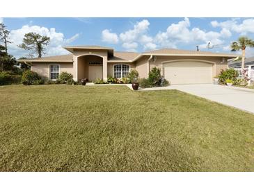Tan house with lush lawn, attached garage, and mature landscaping at 4743 Butterfly Ln, North Port, FL 34288