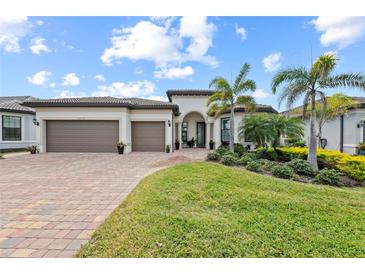 Beautiful single-story home with a three car garage, lush landscaping, and a brick driveway under a sunny blue sky at 13315 Rinella St, Venice, FL 34293