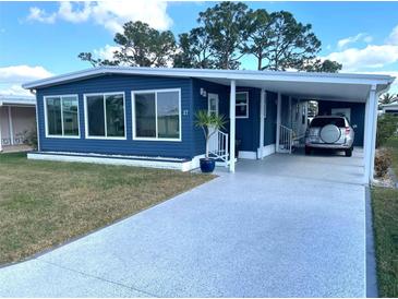 Charming blue home featuring a covered parking area, a well-manicured lawn, and large windows at 17 Nautical Dr, North Port, FL 34287