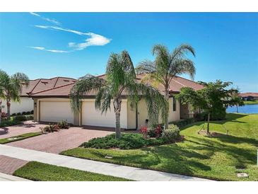 Charming home with a two-car garage, brick driveway, and lush landscaping featuring palm trees and manicured shrubbery at 24065 Canterwood Way, Venice, FL 34293