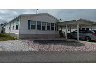 Charming single-story home with white siding, blue shutters, rock landscaping, and a covered carport at 749 N Green Cir, Venice, FL 34285