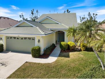 Charming single-story home featuring a light yellow exterior, well-manicured lawn, and a two-car garage with a beautiful garden at 1298 Highland Greens Dr, Venice, FL 34285