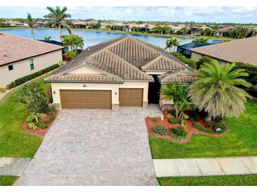 Beautiful lakefront home with a well-manicured lawn, a brick driveway, and a three-car garage at 13238 Famiglia Dr, Venice, FL 34293