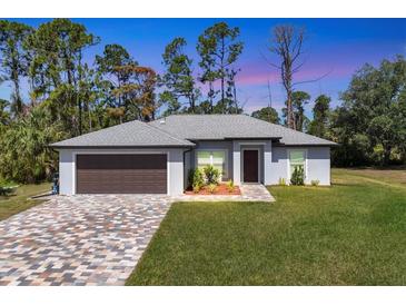 Single-story home featuring a two-car garage and well-manicured lawn at 1449 Overhead St, North Port, FL 34288
