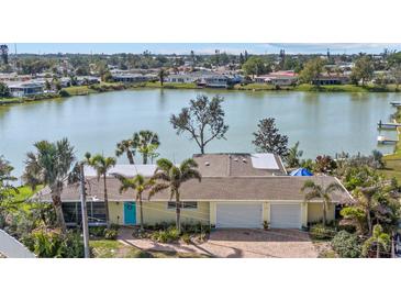 Waterfront home featuring a charming light yellow exterior, attached two car garage, and lush landscaping at 424 Shade Ter, Venice, FL 34293