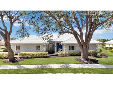 Charming single-story home with a well-manicured lawn, lush landscaping, and a pristine white tile roof at 803 Carnoustie Dr, Venice, FL 34293