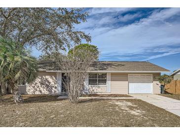 House exterior featuring a one-story light beige house with a white garage door and manicured lawn at 5405 Mariner Blvd, Spring Hill, FL 34609