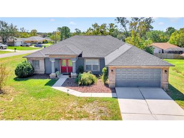 Brick house with gray garage door and red front door, nicely landscaped lawn at 13474 Tune Ln, Spring Hill, FL 34609