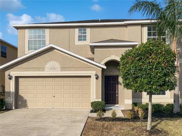 Two-story house with a tan exterior, two-car garage, and manicured lawn at 16617 Magnolia Reserve Pl, Wimauma, FL 33598