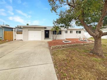 Light beige house with a white garage door, landscaping, and a spacious driveway at 6025 43Rd N Ave, St Petersburg, FL 33709